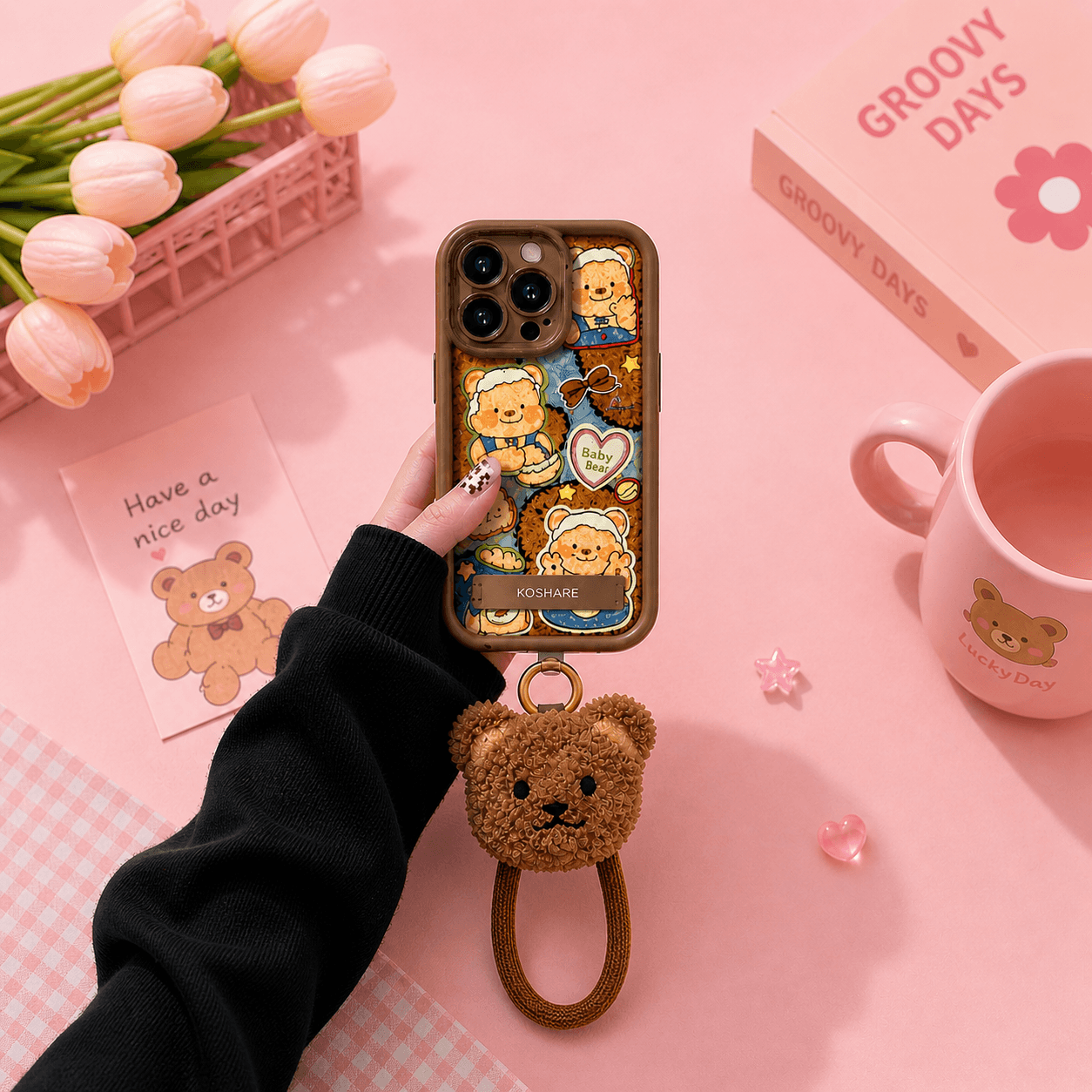 Brown-tinted iPhone case printed with a collage of cartoon teddy bears in blue overalls, stars and hearts, with a fluffy brown teddy bear head charm on a wrist loop