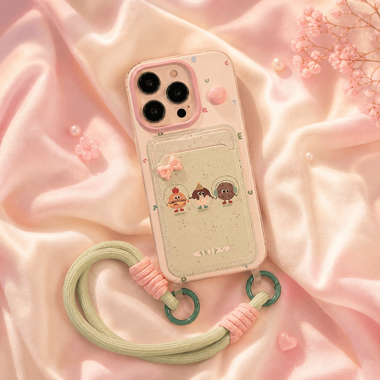 Pink-tinted clear iPhone case with a glitter card-holder pocket, cartoon dessert characters, a pink 3D bow, and a sage green rope wrist strap